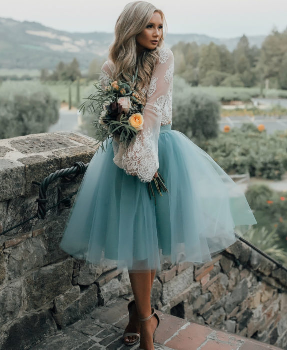 Idéias de vestido de casamento para jardim ao ar livre;  garota com cabelo louro platinado longo ondulado, tule azul falso estilo bailarina e top de renda branca, posando com um buquê de flores