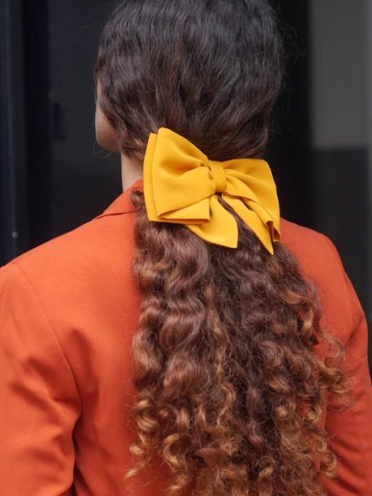 Chca de cabelos compridos cacheados com laço amarelo em um rabo de cavalo