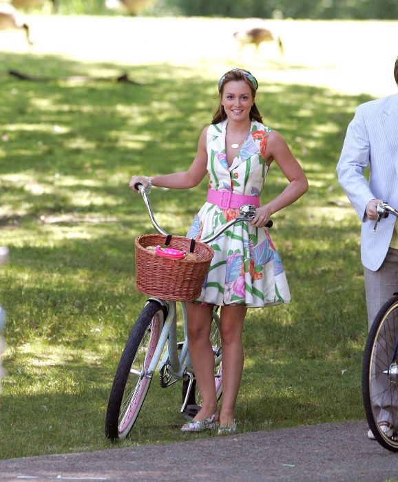 Blair Waldorf usando um vestido florido com um cinto rosa enquanto segura uma bicicleta 