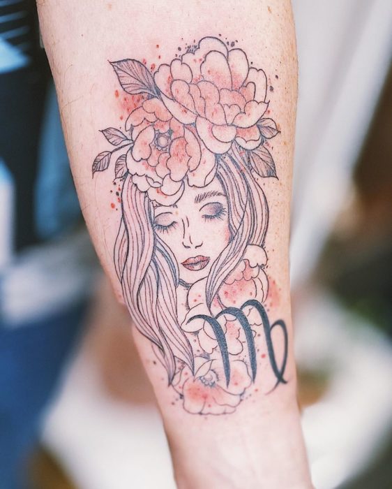 Tatuagem do rosto de uma mulher e o símbolo da virgem na área do antebraço