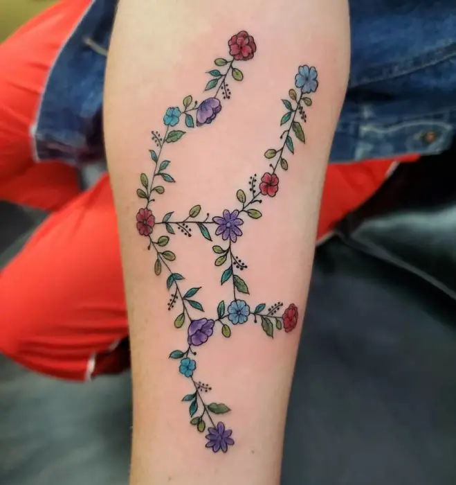 Tatuagem da constelação de Virgem feita com flores e cores na área do antebraço