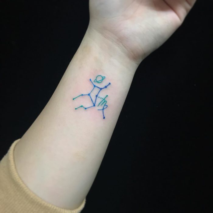 Tatuagem da constelação de Virgem com tinta azul na área do pulso