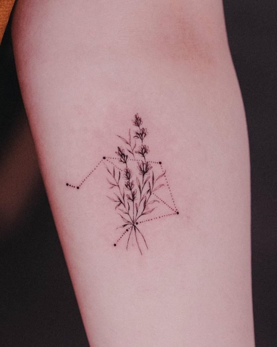 Tatuagem da constelação de Libra adornada com um ramo de vegetação na área do antebraço
