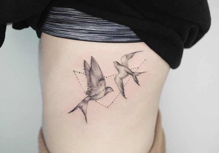 Tatuagem de constelação de Capricórnio com duas andorinhas na lateral do abdômen