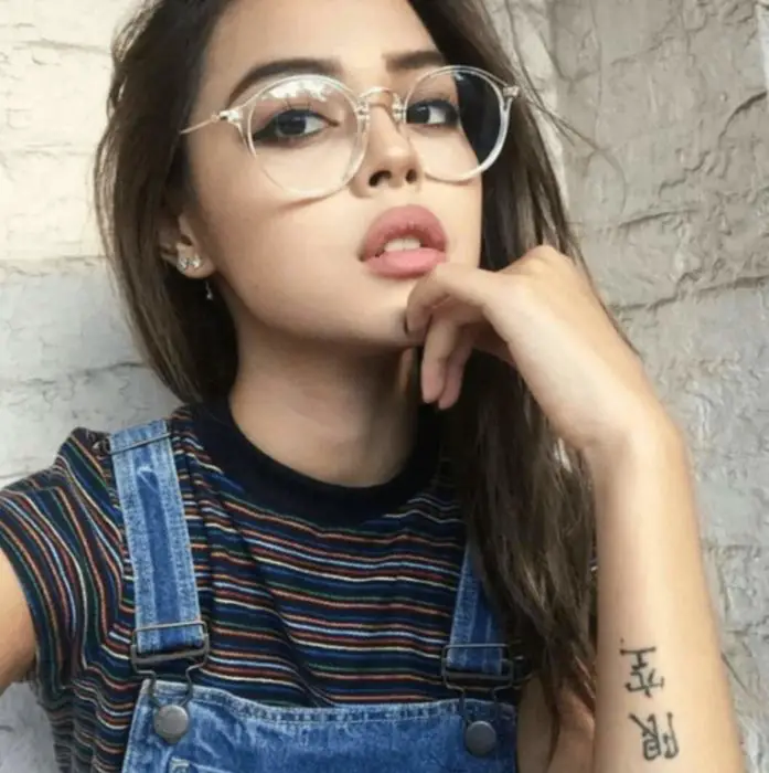 Garota posando para uma foto enquanto mostra seus pequenos óculos redondos transparentes