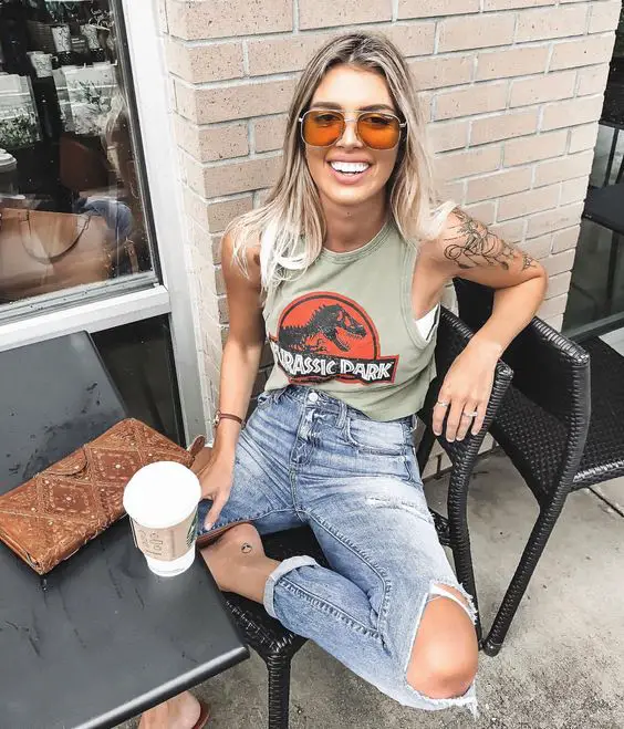 Garota fora de um café, sentada, sorrindo, vestindo roupas com camiseta do Jurassic Park