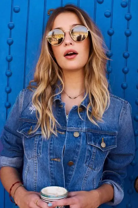 Garota recarregada em uma parede azul modelando sua roupa e óculos redondos