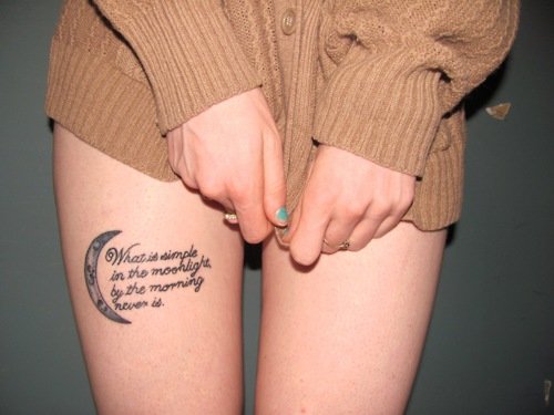 garota com uma frase tatuada na perna vestindo apenas um suéter 