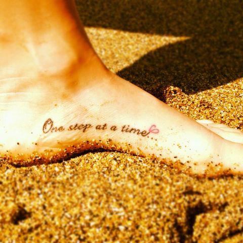 garota com um pé tatuado com uma frase que está na areia 