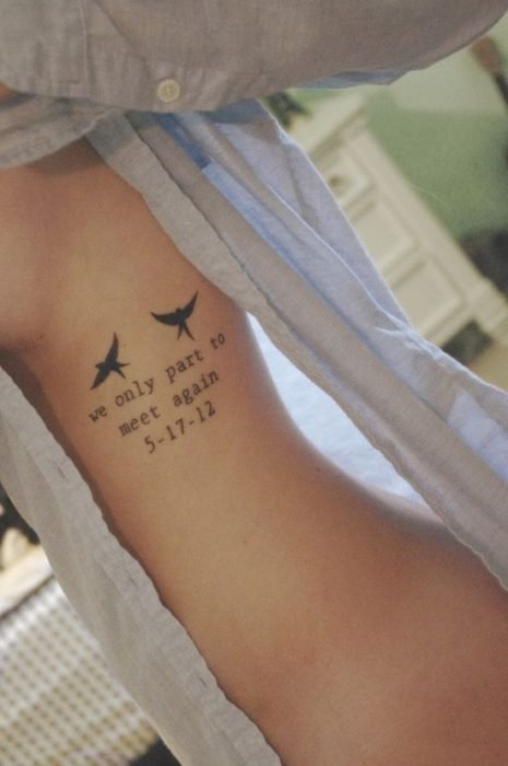 Menina com uma blusa azul mostrando sua tatuagem que é uma frase com dois pássaros 