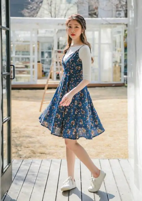 Looks com vestidos e blusas básicas;  Mulher coreana com penteado meio rabo de cavalo com tranças, vestido flor azul com blusa branca de manga curta e tênis