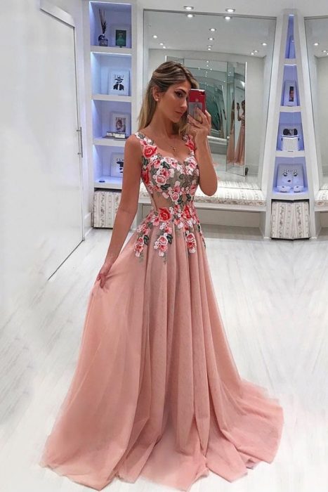 Menina tirando uma foto com o celular, modelando um vestido rosa transparente com detalhes de flores
