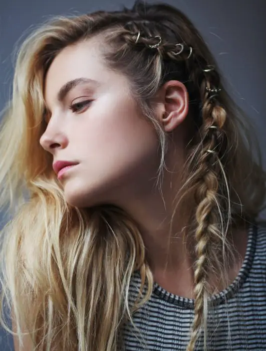 Rapariga loira com cabelo solto e uma trança lateral penteada com anéis ao estilo viking
