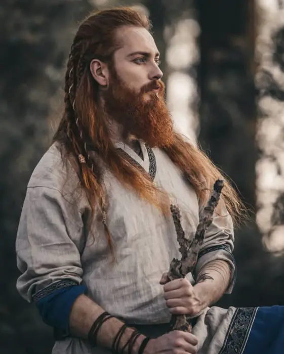 Homem ruivo com cabelo comprido e penteado com tranças, aparência viking, com barba cerrada e bigodes