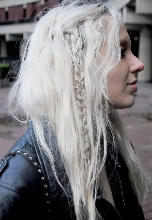Menina com cabelos brancos desgrenhados, com trança adornada com anéis