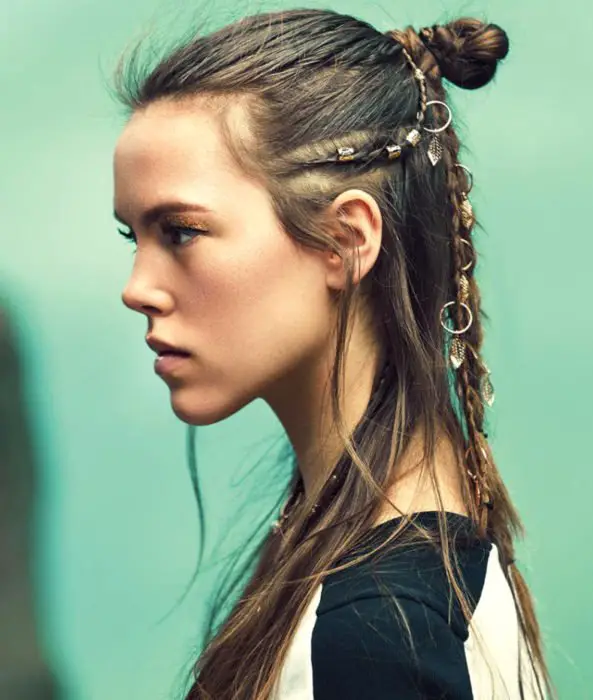 Menina com cabelos castanhos lisos estilo Lagertha dos Vikings, com tranças, anéis e meio coque