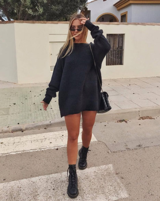 Menina atravessando a rua, vestindo um suéter cinza grande demais como vestido curto de outono, com botas de trabalho Dr. Martens 