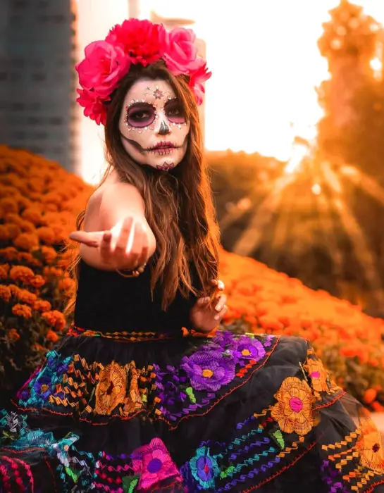Maquilhagem tradicional da Catrina para o Dia dos Mortos com coroa de flores na cabeça e strass;  Menina desaparecida com flores bordadas em um campo de calêndula 