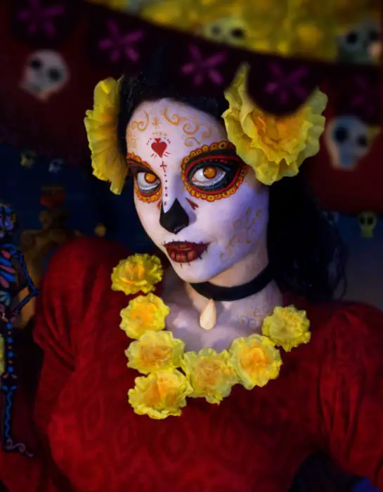 Modern Day of the Dead Catrina maquiagem com flores de calêndula amarela com um vestido vermelho;  mulher disfarçada de livro da vida