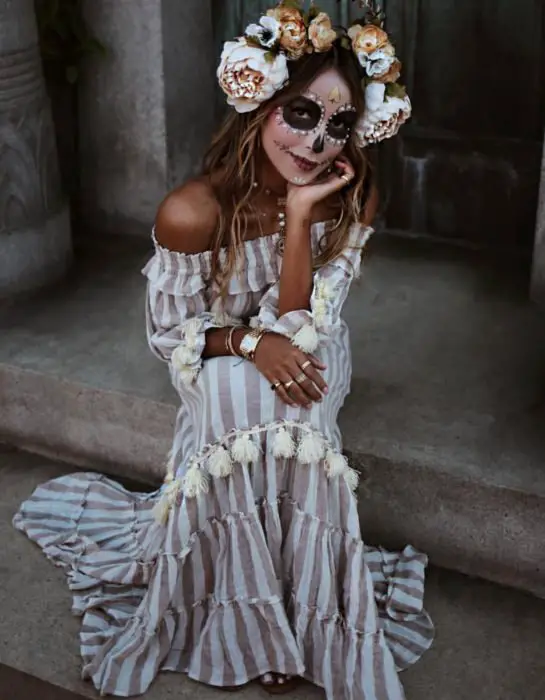 Modern Day of the Dead Catrina maquiagem ouro;  menina sentada na escada em vestido maxi listrado vertical sem ombros, branco e marrom;  flores na cabeça