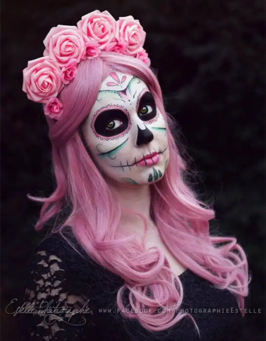 Maquilhagem moderna de Catrina para o Dia dos Mortos;  menina com cabelo longo rosa ondulado, coroa de flores e blusa de renda preta