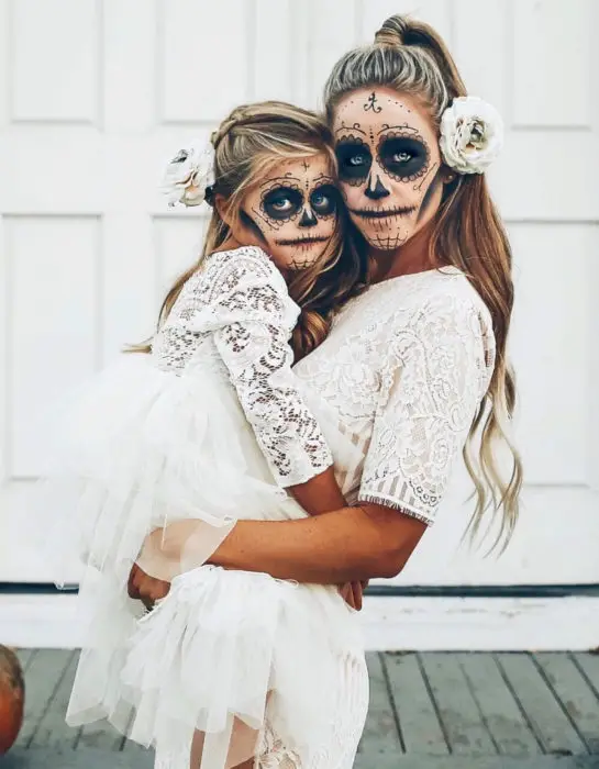 Modern Day of the Dead Catrina maquiagem;  mãe e filha vestidas de caveiras com vestidos de renda branca e flores no cabelo 