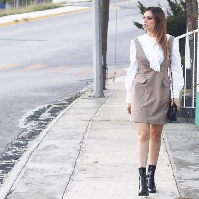 Menina andando na rua com um vestido marrom e uma blusa branca combinada com botins pretos 