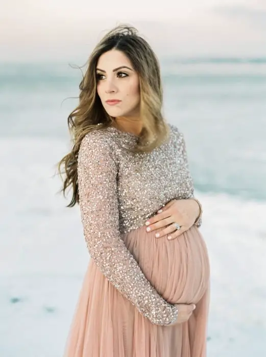 Vestidos de chá de bebê, sessão de fotos de gravidez na praia, mulher loira de cabelo comprido com vestido rosa salmão e blusa de lantejoulas de manga comprida