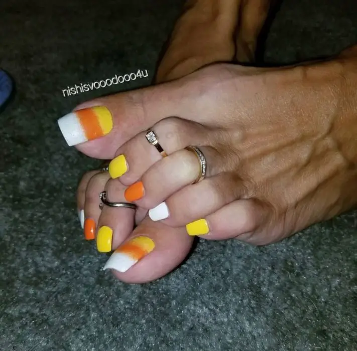 Menina com unhas de acrílico nos pés em branco, laranja e amarelo 