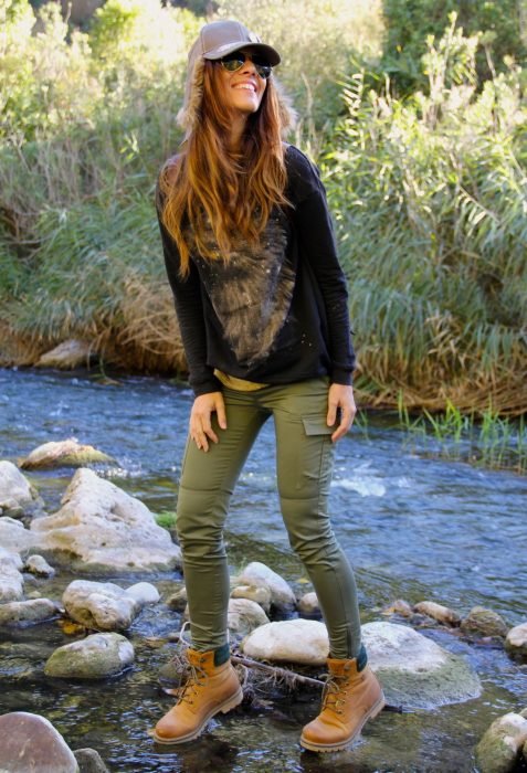 Menina de pé nas pedras de um rio, vestindo uma roupa verde e botas Timberland 