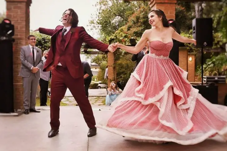 Um casal de noivos dança no chão, ela em um vestido vermelho com chiffon branco por cima