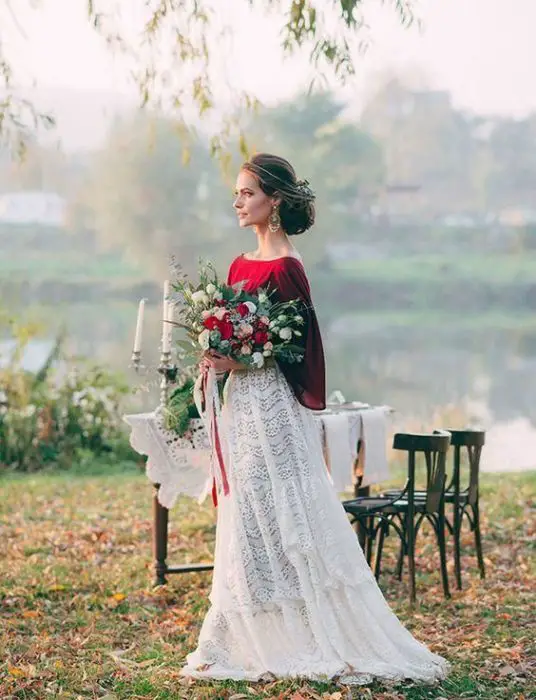 uma noiva em um vestido branco e vermelho perto de uma mesa decorada perto de um lago no campo