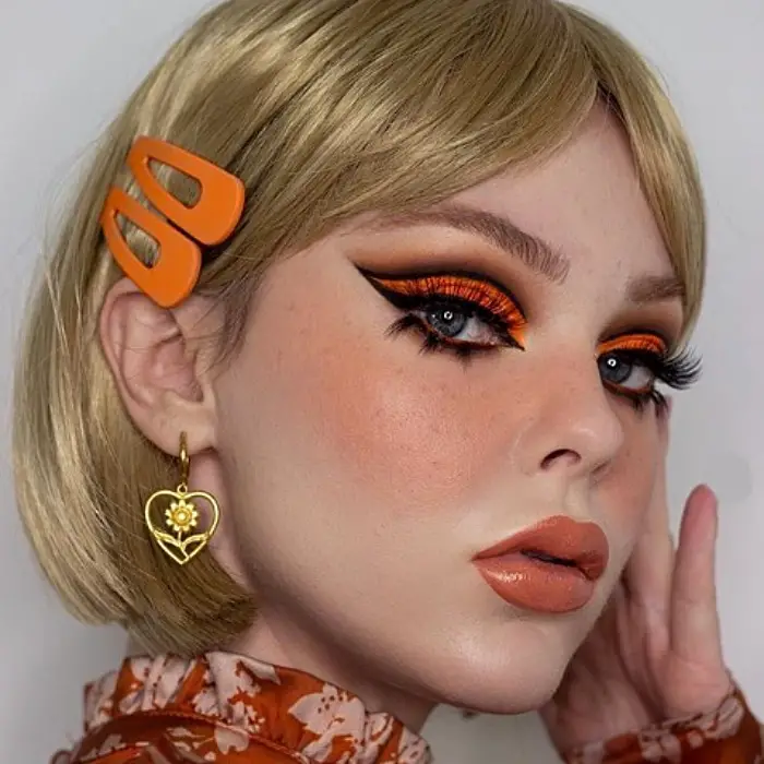 menina loira com maquiagem dos anos 60, sombra laranja, delineador preto, batom laranja 