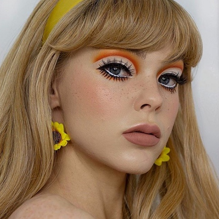 menina com longos cabelos loiros, usando maquiagem dos anos 60, contornado em laranja, cílios postiços, brincos de girassol