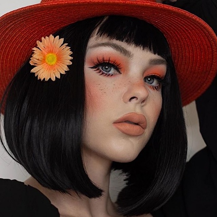 menina com cabelo preto, chapéu vermelho, sombra laranja, delineador preto e batom neutro