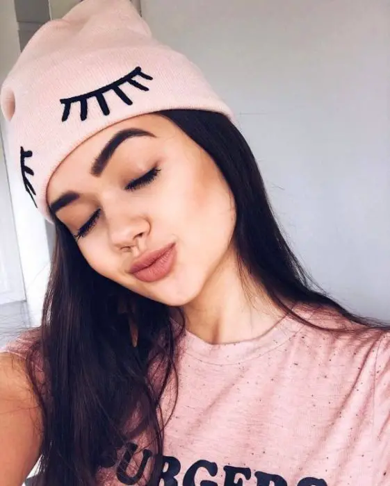 Menina com os olhos fechados inclinando a cabeça com um chapéu rosa pastel
