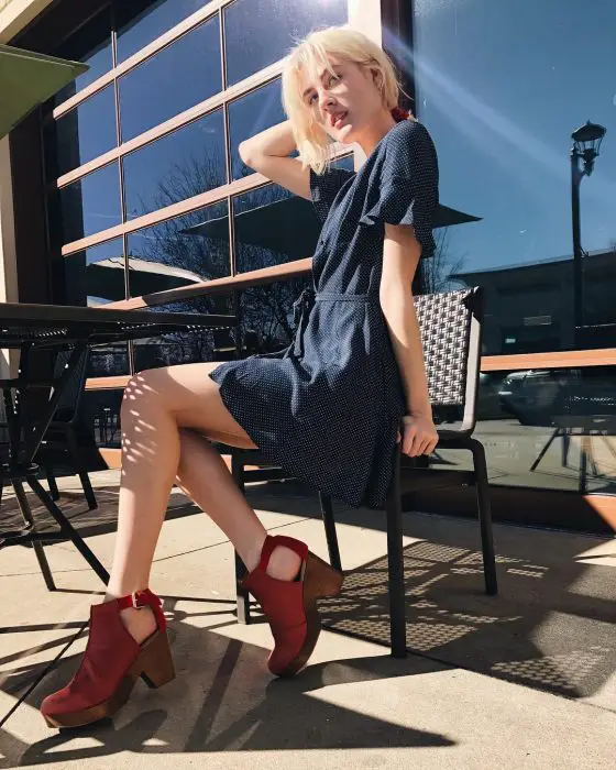 Menina sentada em um café mostrando seus sapatos vermelhos