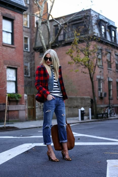 Rapariga loira com um casaco xadrez, uma camisa listrada, calça jeans, salto com estampa animal na rua
