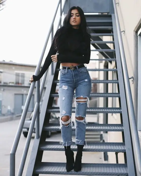 Menina na escada com blusa preta, jeans rasgado e salto preto